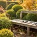 Jardin d’automne lumineux avec des vivaces rabattues et des outils de taille posés sur un banc en bois.
